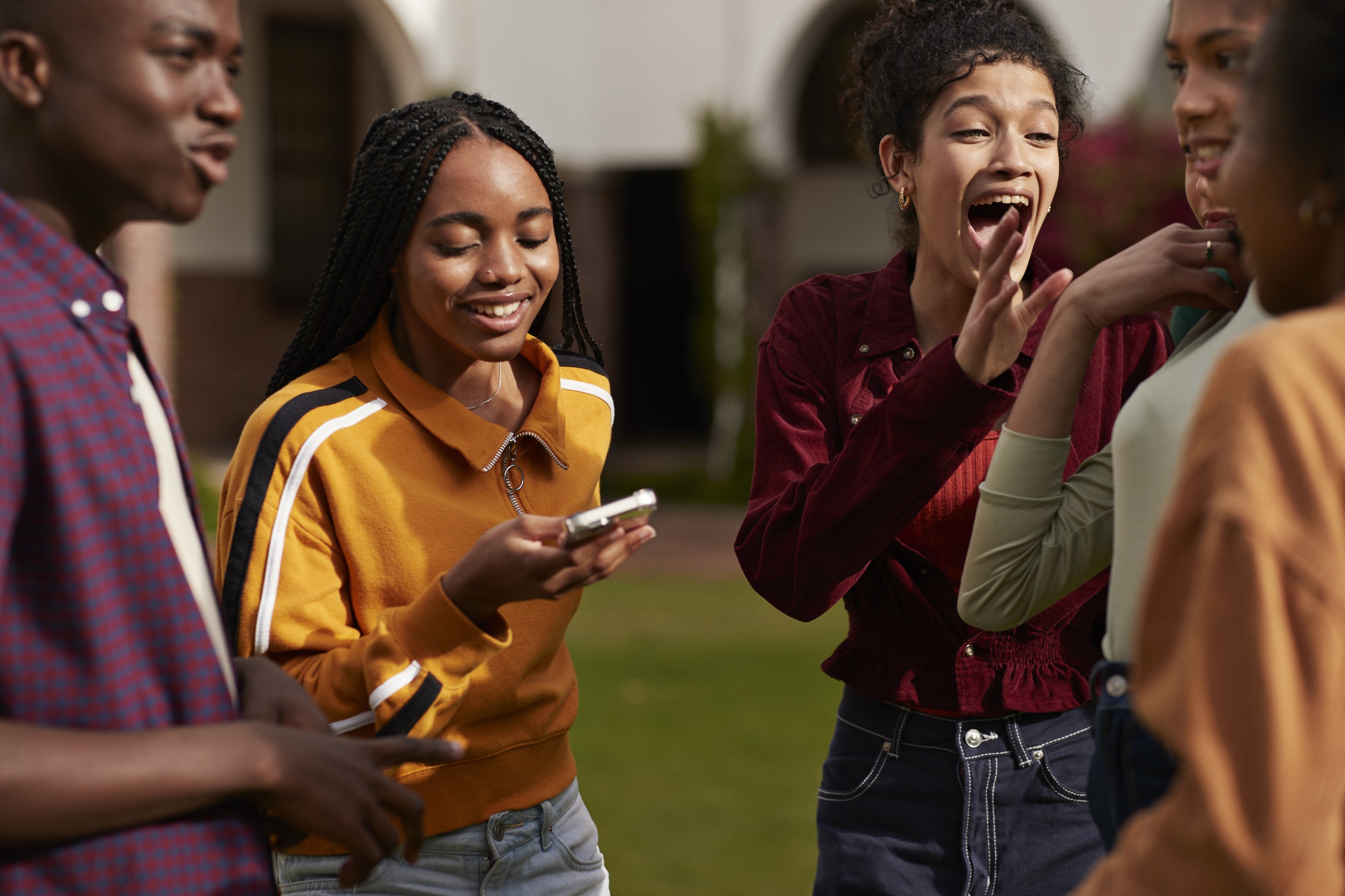 Trans person using smart phone amidst friends enjoying break at campus in high school